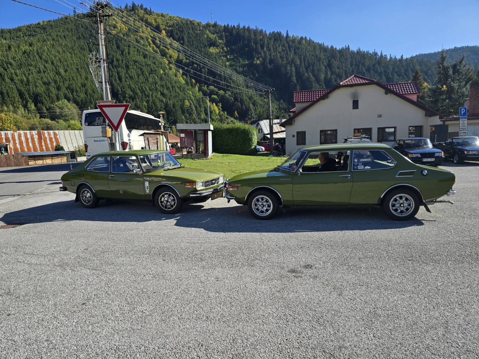 Zwei grüne Saab 99 stehen einander vor einer Bergkulisse gegenüber